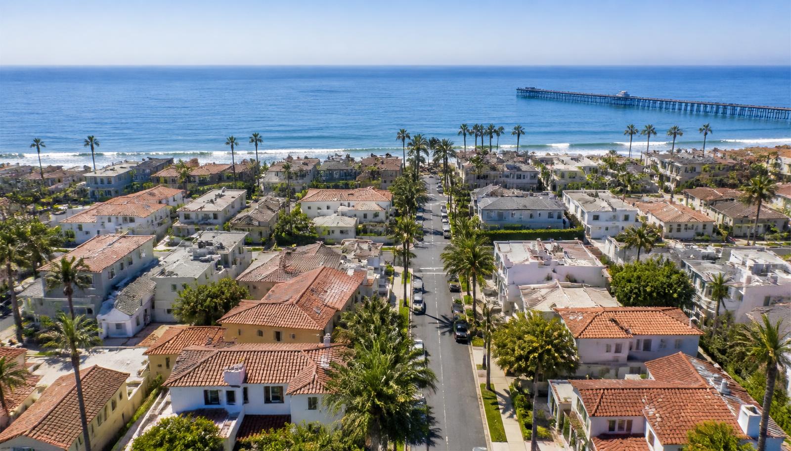 Aerial view of a palm-lined Orange County coastal neighborhood with the pier in the distance